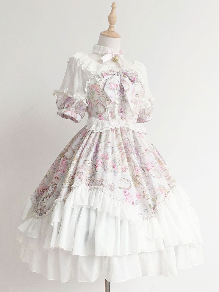 a white lolita fashion dress is shown on a mannequin against a white background. the dress is shortsleeved and falls to just below the knee. it features a floral print, lace trim, and ruffles. the bodice is fitted and the skirt is full.