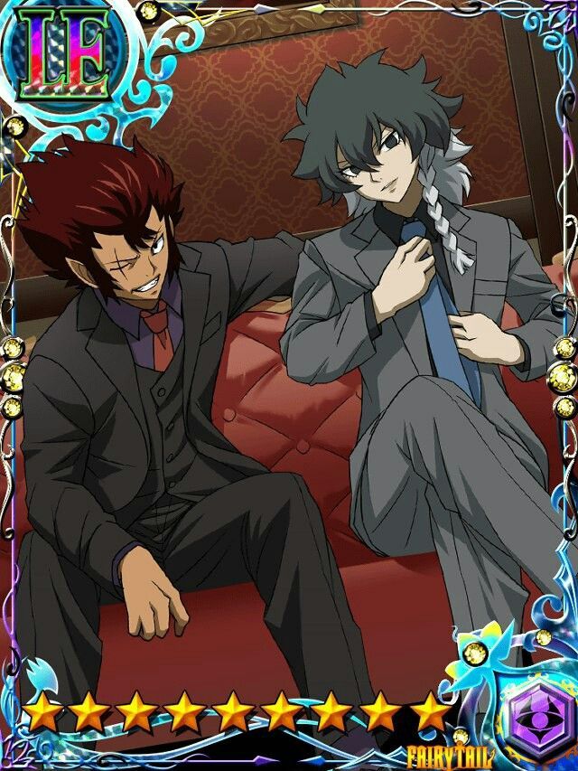 this image shows a card for the game "fairy tail" featuring natsu dragneel and gajeel redfox. natsu is on the left, wearing a black suit with a red tie. gajeel is on the right, wearing a gray suit with a blue tie. they are both sitting on a red couch in a room. the card is surrounded by a gold frame with stars and a "fairy tail" logo.