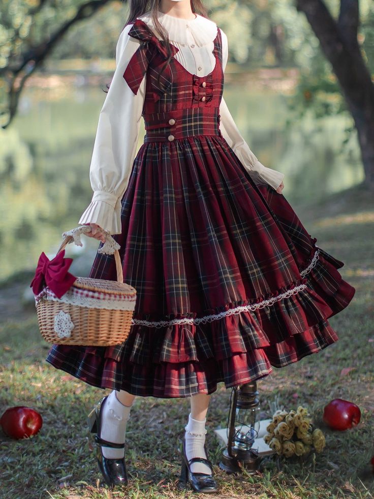 a woman in a red and black plaid lolita fashion dress stands in a forest. she is holding a wicker basket with a red bow. there are apples and a lantern on the ground near her. the lighting is soft and natural, and the perspective is eyelevel.