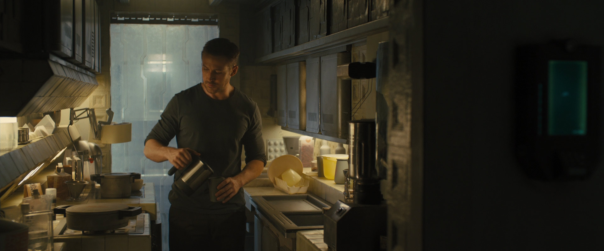 a man is standing in a dark kitchen, making coffee. he is pouring coffee from a coffee pot into a cup. there is a coffee machine on the counter, and shelves behind him are stacked with food and other supplies. the kitchen has a dark, moody atmosphere.
