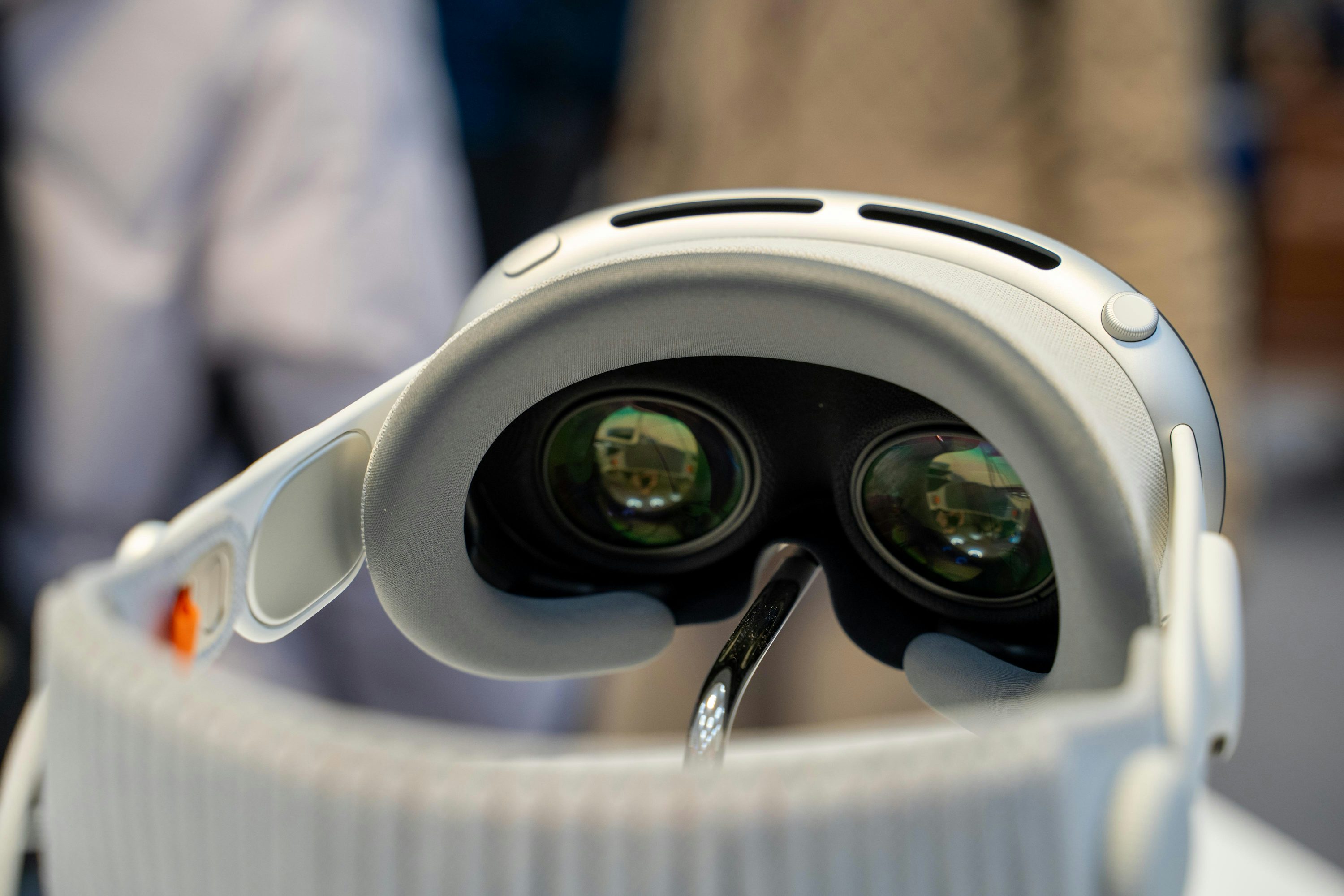 a closeup shot of a meta quest pro vr headset. the headset is white and grey with visible lenses and padding. the head strap and ventilation slots are also visible.