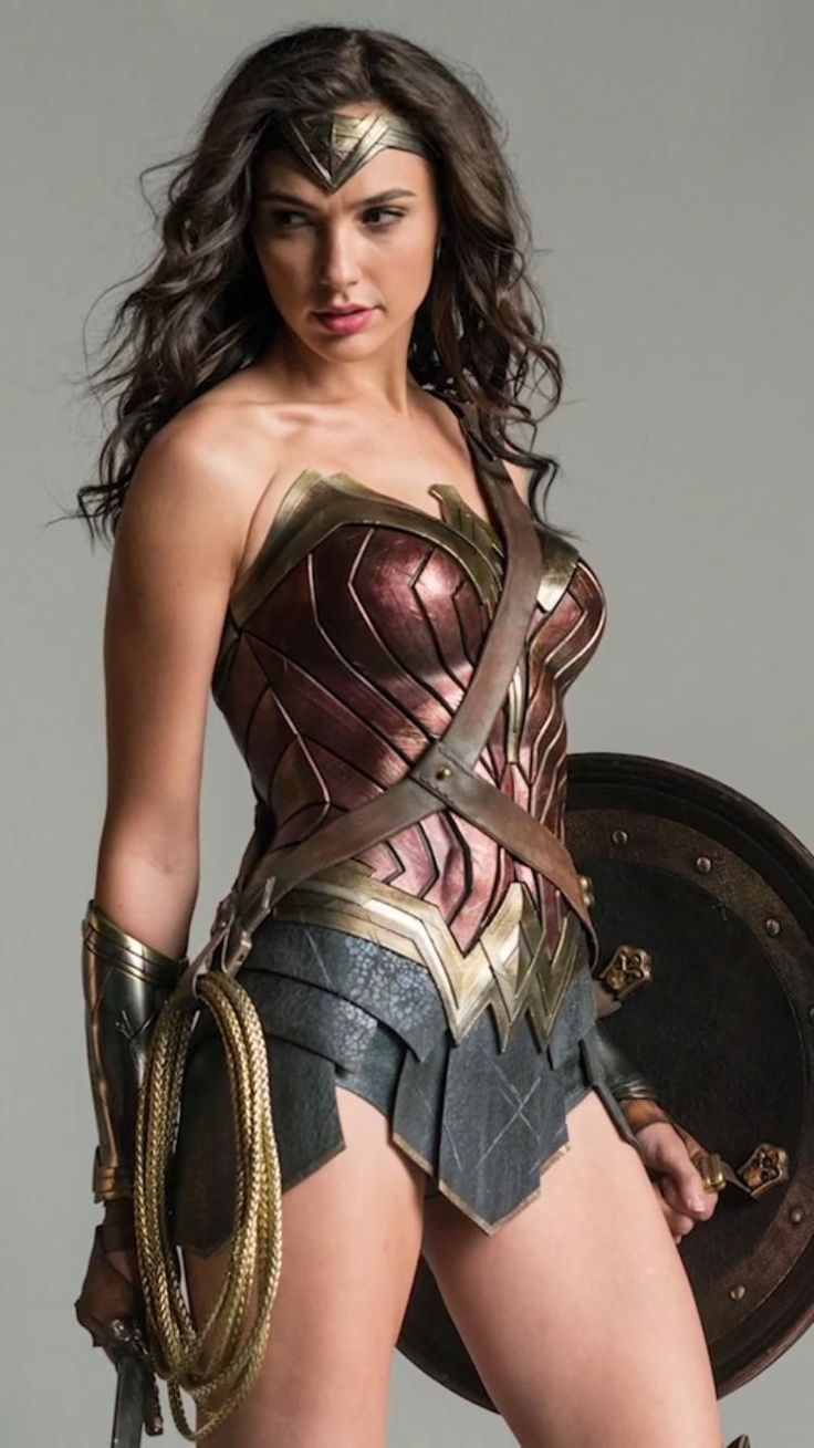wonder woman, played by gal gadot, stands with her shield and sword in hand, looking fierce and powerful. she is wearing her iconic costume, complete with the golden tiara, bracelets, and the red and gold breastplate. the image captures the essence of wonder woman's strength and beauty, making her a compelling and inspiring figure.