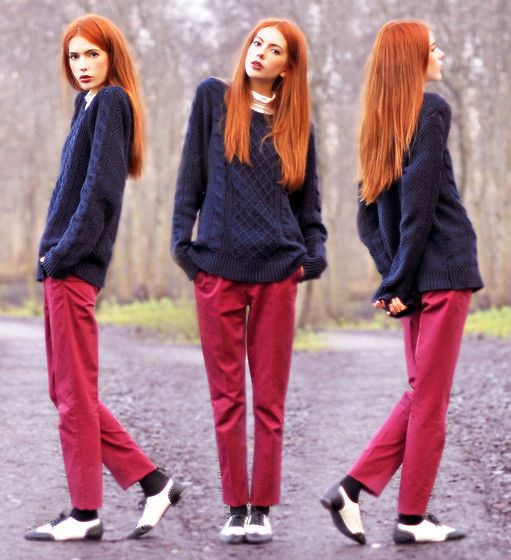 a triplicate image of a young woman with long, vibrant red hair. she is wearing a dark blue cableknit sweater, crimsoncolored trousers, and white saddle shoes. the setting appears to be outdoors in a parklike environment with trees and a gravel path. the woman is posed in slightly different positions in each of the three images. the overall style is casual yet chic, suggesting a fall or winter outfit.