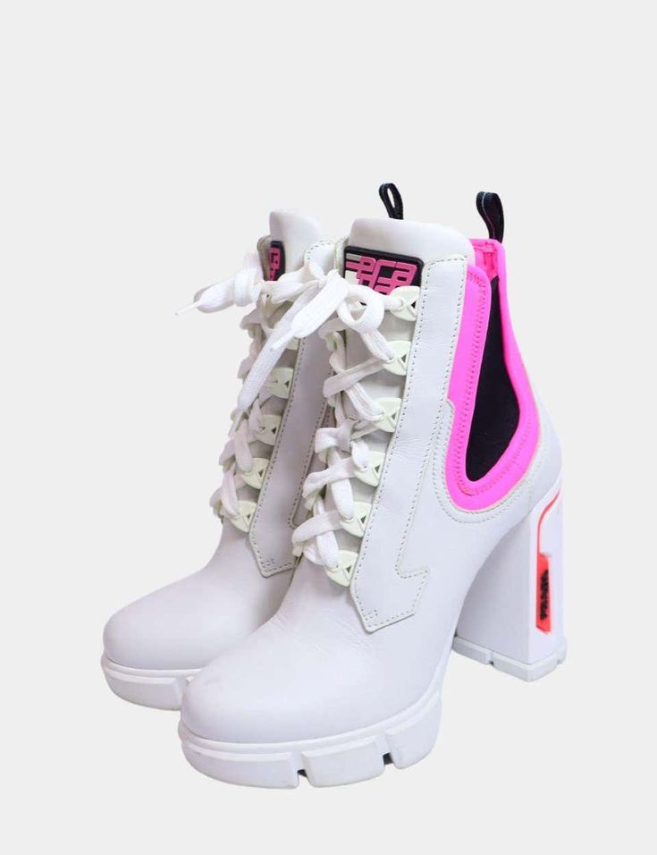 a pair of white prada ankle boots with pink accents are shown in this image. the boots are laceup and have a chunky heel. they appear to be made of leather and have a platform sole.