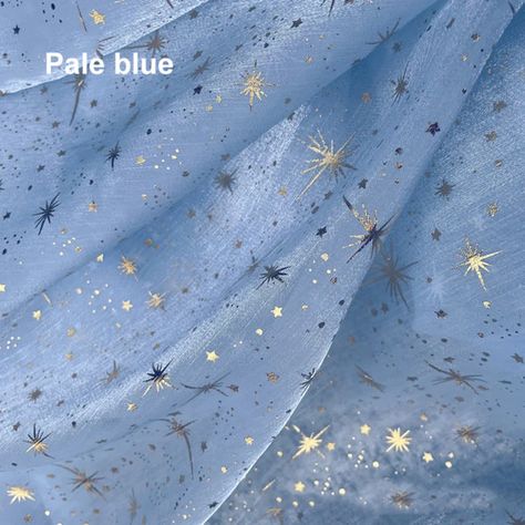 a close up photograph of pale blue fabric printed with gold stars. content: fabric, starspeople: environment:lighting: soft, diffused perspective: close upkw: fabric, textile, sewing, craft, fashion, star, blue, gold, pale, pastel, iridescent, ethereal, dreamy