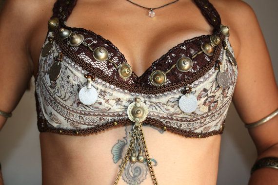 a woman is wearing an ornate belly dancing bra with silver and gold coins and jewelry. the bra is a brown and white patterned design and is a traditional costume for belly dancing. the woman is also wearing a silver chain around her neck.