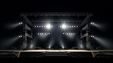 the image shows a stage with a metal truss structure, bright lights, and a platform. the stage is set for a concert or performance. the overall tone of the image is dark, emphasizing the lighting.