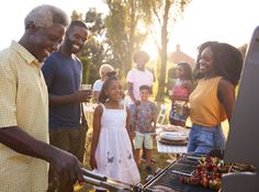 a photo of a happy multigenerational family grilling food and enjoying a barbecue outside in their backyard. the sun is setting, casting a warm glow on the scene.