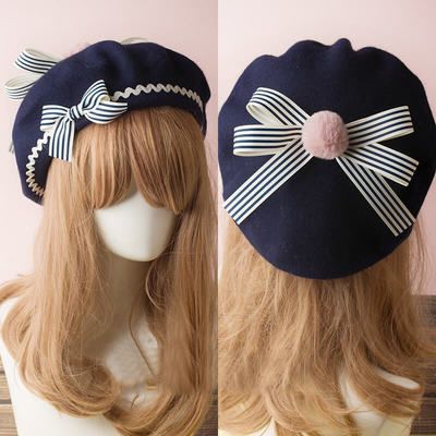 the image showcases a navy blue beret adorned with white ribbons featuring blue stripes. a charming pink pompom sits atop the beret, adding a touch of whimsy. the beret is displayed on a model with long, flowing blonde hair, providing a clear view of both the front and back of the stylish headwear.