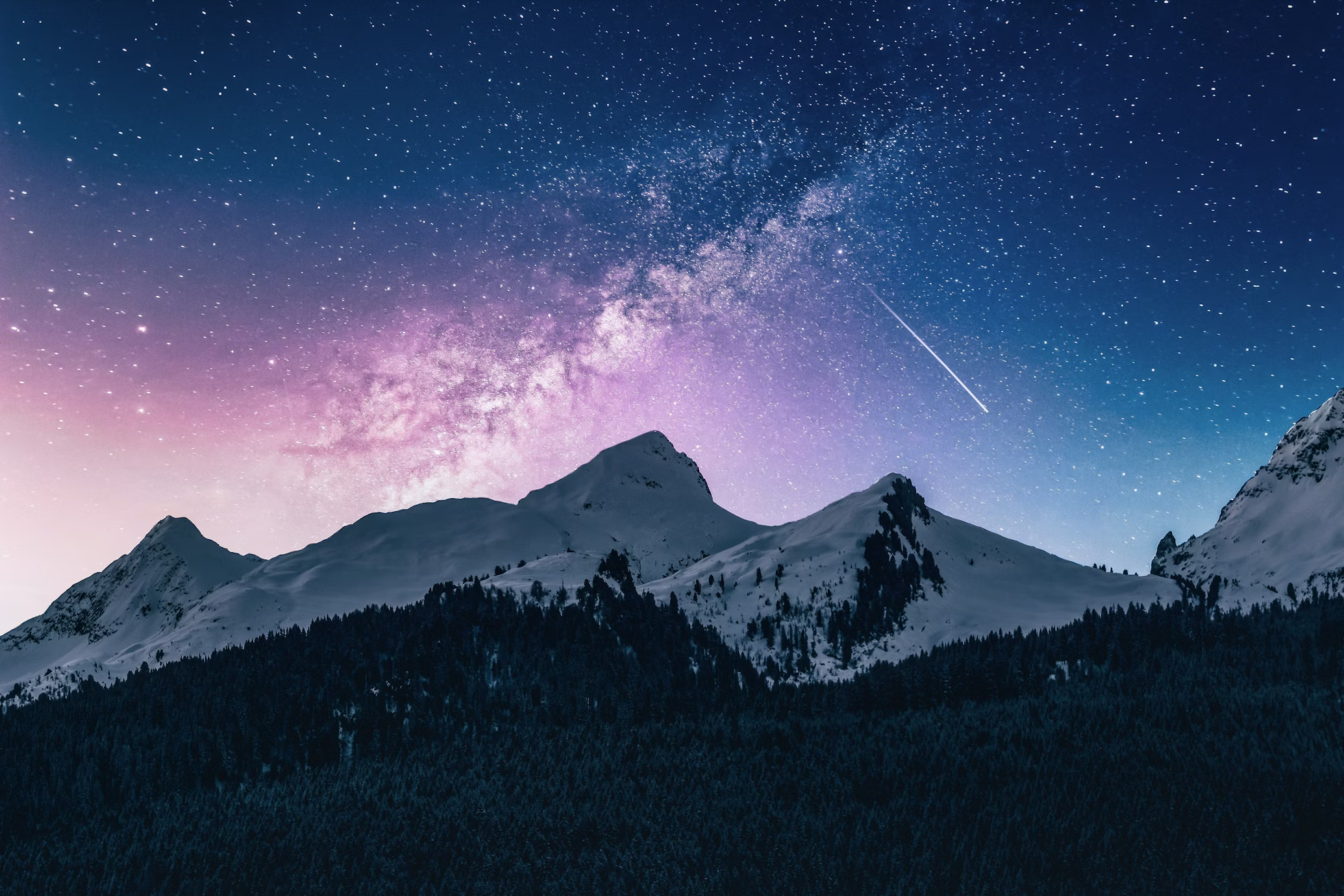 the image shows a majestic snowcapped mountain range set against a breathtaking backdrop of a starfilled night sky. the milky way galaxy is prominently displayed, stretching across the heavens in a mesmerizing swirl of stars and cosmic dust. a shooting star streaks across the sky, adding a touch of magic to the scene. the foreground features a dark and dense forest, creating a sense of depth and contrast.