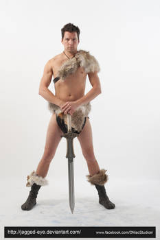 a fullbody shot of a muscular male model posing in a barbarian costume. he is wearing a fur shoulder piece and leg warmers. he is holding a large sword with both hands, standing with his legs apart. the background is white. the image is a studio shot and looks to be a stock photo for use in fantasy or medieval settings.
