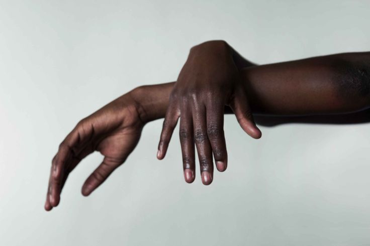 a closeup of a darkskinned person's hand reaching out towards the viewer, with the arm extended and the fingers outstretched. the hand is slightly curled, as if in a gesture of reaching or touching. the skin is visible and has a natural, slightly textured appearance.