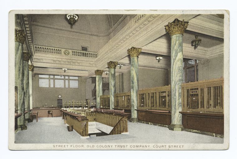 this image is a vintage postcard depicting the interior of the old colony trust company on court street. the view shows the street floor of the bank, featuring marble columns with ornate capitals. rows of teller windows line the right side of the frame. the mezzanine is visible at the top of the image, and a vault entrance is in the foreground. architectural details, such as lighting fixtures, are prominent.