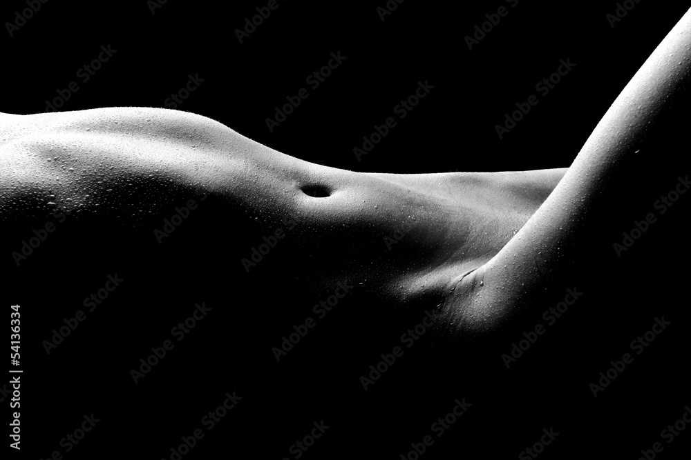 a black and white closeup photograph of a woman's torso, showing her abdomen, navel, and the subtle curves of her body. the lighting creates a strong contrast between the highlights and shadows, emphasizing the texture of the skin, which appears slightly wet or sweaty. the overall tone is sensual and artistic, with an emphasis on the form and shape of the body. the image is shot against a dark background, enhancing the dramatic effect.