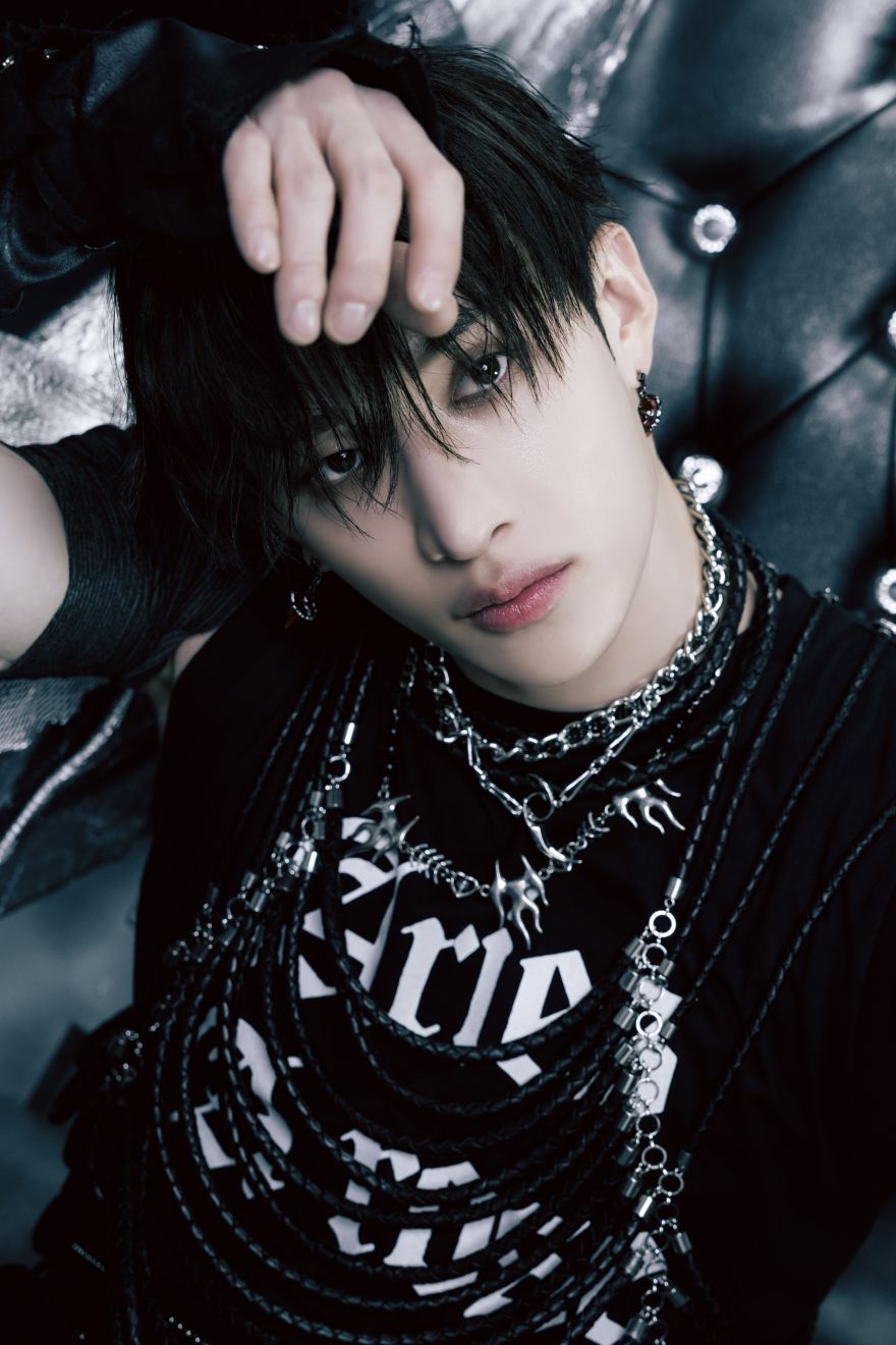 closeup portrait of a young kpop male idol with dark black hair, wearing numerous layered necklaces and leather accessories.  he has a serious and intense expression. the background is dark and moody, emphasizing the edgy and gothic style of the image.  the overall aesthetic is dark, rebellious, and stylish, typical of a kpop photoshoot.