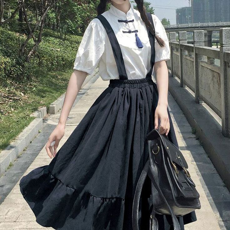 a young woman stands on a paved path, posing for a photo. she wears a stylish outfit that blends modern and traditional elements. her black, full skirt features a ruffled hem and pairs with a white, shortsleeved top accented with a high collar and frog closure. a black backpack hangs from her shoulder. the surrounding environment suggests an urban park setting, with lush greenery, a bridge in the background, and dappled sunlight filtering through the trees.
