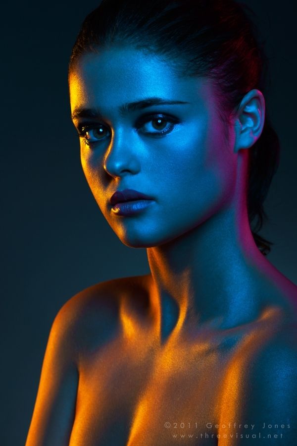 a closeup portrait of a beautiful woman with bright blue, yellow, and magenta lighting highlighting her skin, eyes, and lips.