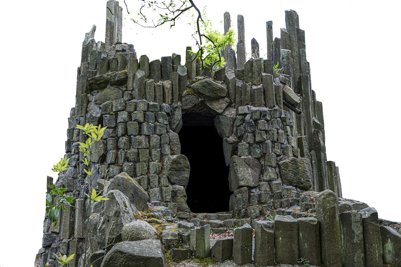 a stone structure resembling a castle ruin with basalt columns stands in a park. the structure is made of gray stone and features an archway leading to a dark interior. greenery, including trees and plants, surrounds the structure. it looks like the kromlau rakotzbrucke.