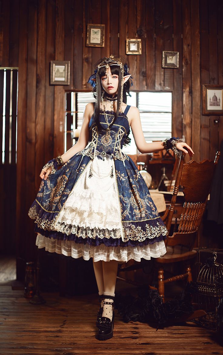 a woman in a blue and white lolita dress, with a crown,  stands in a room with an antique chair and cage. she is looking to the side with her head tilted. the room is decorated with wooden walls and a lot of antique decor.