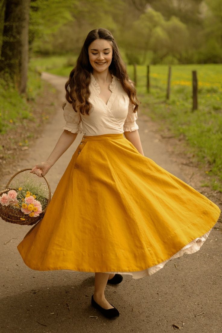 a woman in a vintageinspired outfit twirls on a path in the woods. she is wearing a white blouse and a long yellow skirt with a full petticoat underneath. she is carrying a basket of flowers in one hand. the path is lined with trees and there is a field in the background. the lighting is natural and the perspective is at eye level. the image has a romantic and whimsical feel.