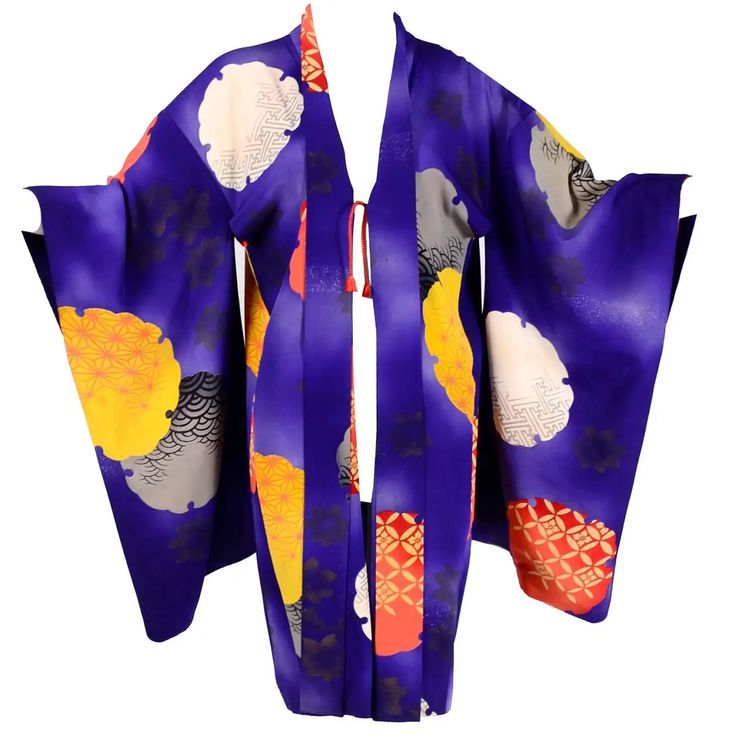 an image of an open front kimono. the kimono is purple with large yellow, red, and gray geometric and floral patterns. the sleeves are wide and the front is open, revealing a red tie.