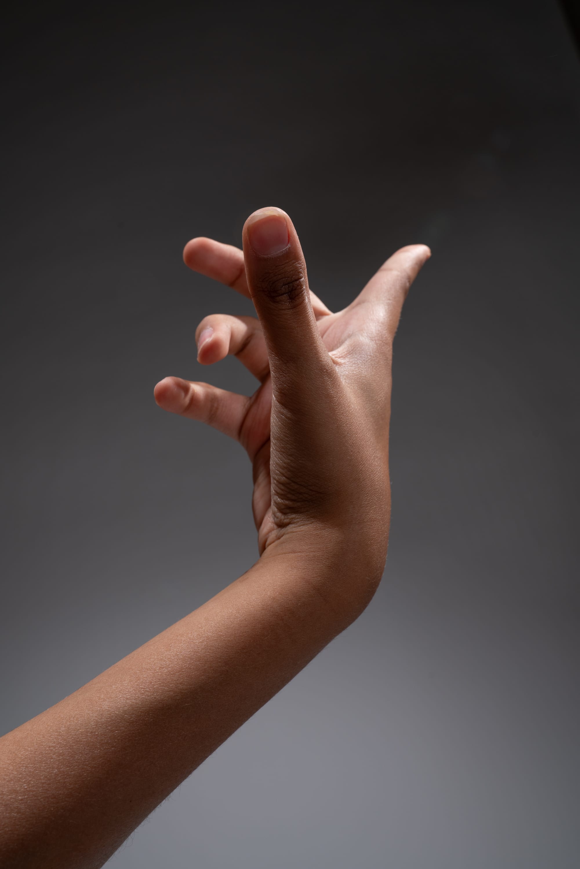 a closeup, lowangle view of a black hand and arm extended upward against a dark gray background, illuminated by studio lighting.  the hand is posed with fingers slightly curled.