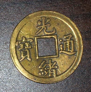 a closeup image of a chinese copper coin. the coin is round with a hole in the center and is inscribed with chinese characters. the coin is in good condition and appears to be quite old. the coin's background is blurred, making it appear as if it is laying on a wooden table.  the coin appears to have a patina of age and wear on its surface.