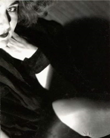 the image is a dramatic, closeup black and white portrait of a woman.  she is partially obscured by shadows, creating a sense of mystery. her face is the focal point, showing expressive eyes and a slightly pensive expression. her dark hair is styled in waves, and she is wearing dark clothing. the lighting is stark, highlighting the contours of her face and the texture of her clothing. the overall mood is sensual and slightly melancholic, reminiscent of film noir aesthetics.