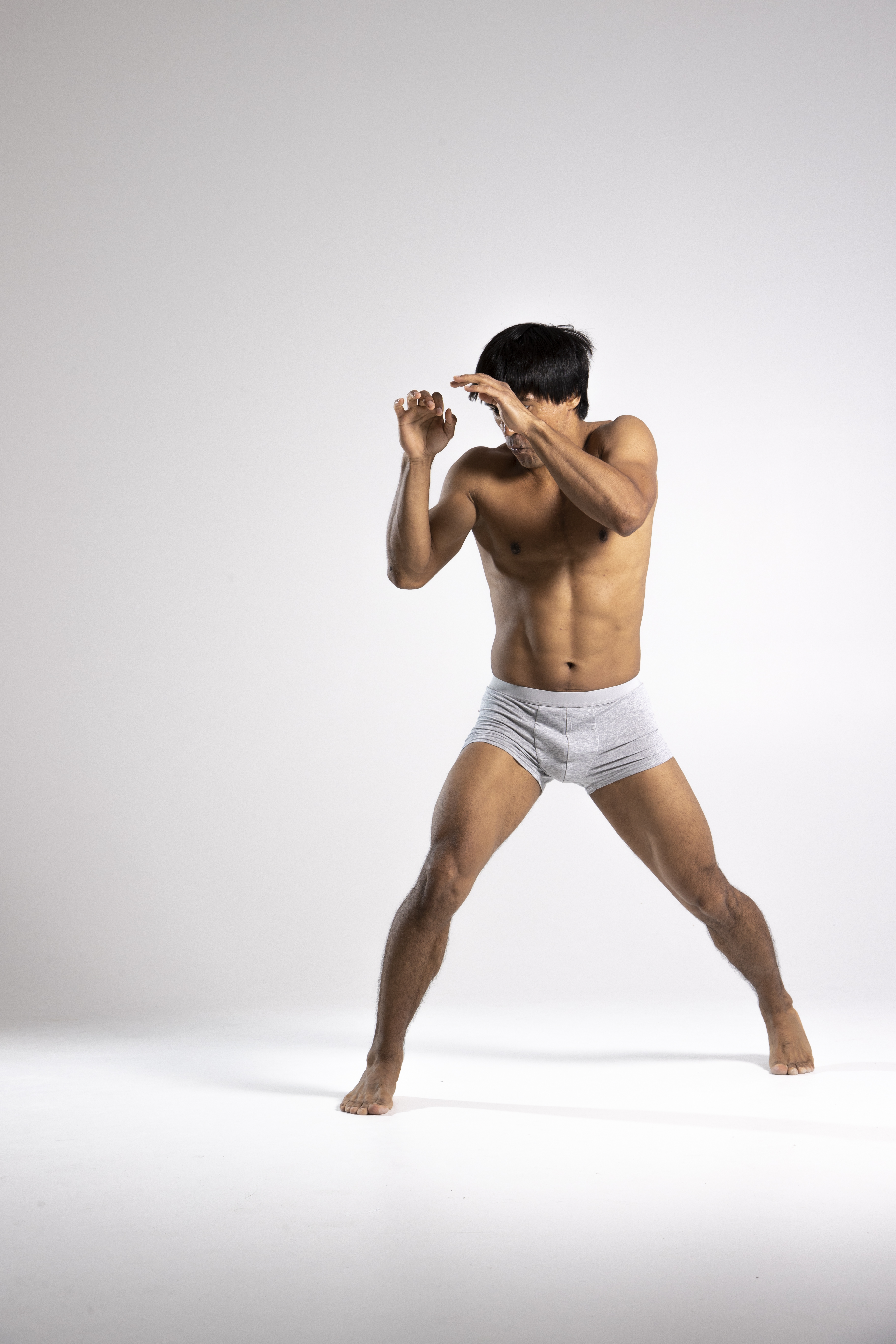 a shirtless man wearing underwear is in a fighting stance. he is defending himself by raising his hands in front of his face.