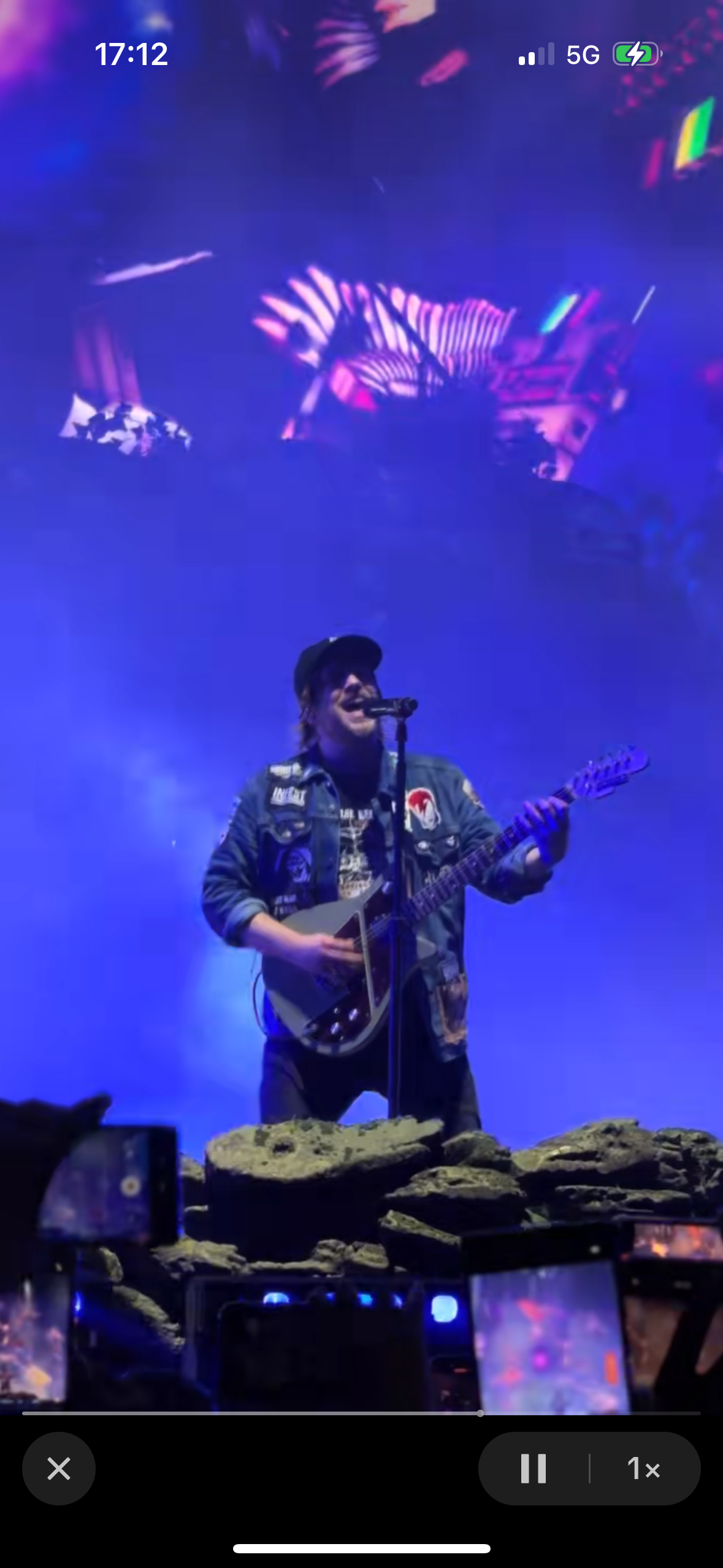 a musician is performing on stage at a concert,  playing a guitar and singing into a microphone. the stage is lit up with spotlights, and there is a crowd of people in the background. the musician is wearing a jean jacket and jeans. the image is taken from the front row of the concert.