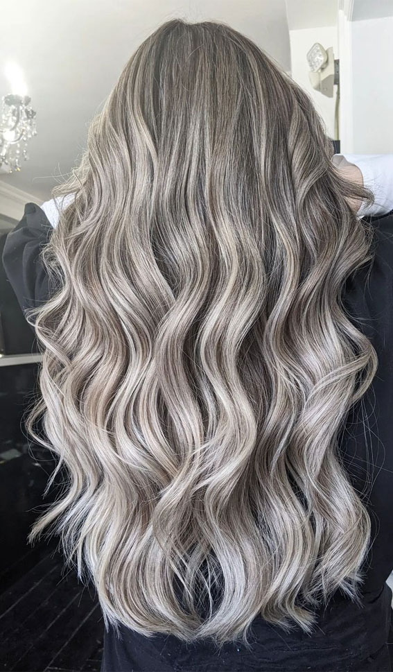 the image showcases the back of a woman's head, highlighting her long, wavy, and blonde hair. the hair has been styled with loose waves, creating a voluminous and flowing effect. the photo is likely taken in a hair salon, as suggested by the indoor lighting and the woman's black attire. the overall image emphasizes the beauty and style of the woman's hair.