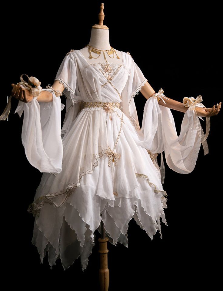 a white chiffon dress with gold trim is displayed on a mannequin. the dress features a vneckline, flowing sleeves tied with ribbons, a gold belt, and a layered skirt with ruffles and petallike hems. a gold necklace is also visible on the mannequin. the background is black.