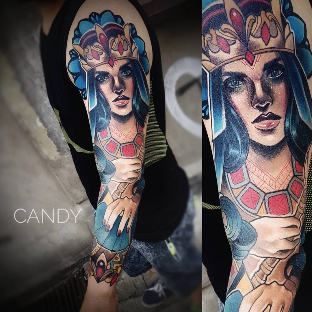 a man with a colorful detailed tattoo of a woman wearing a crown on his left arm. the background is blurred.