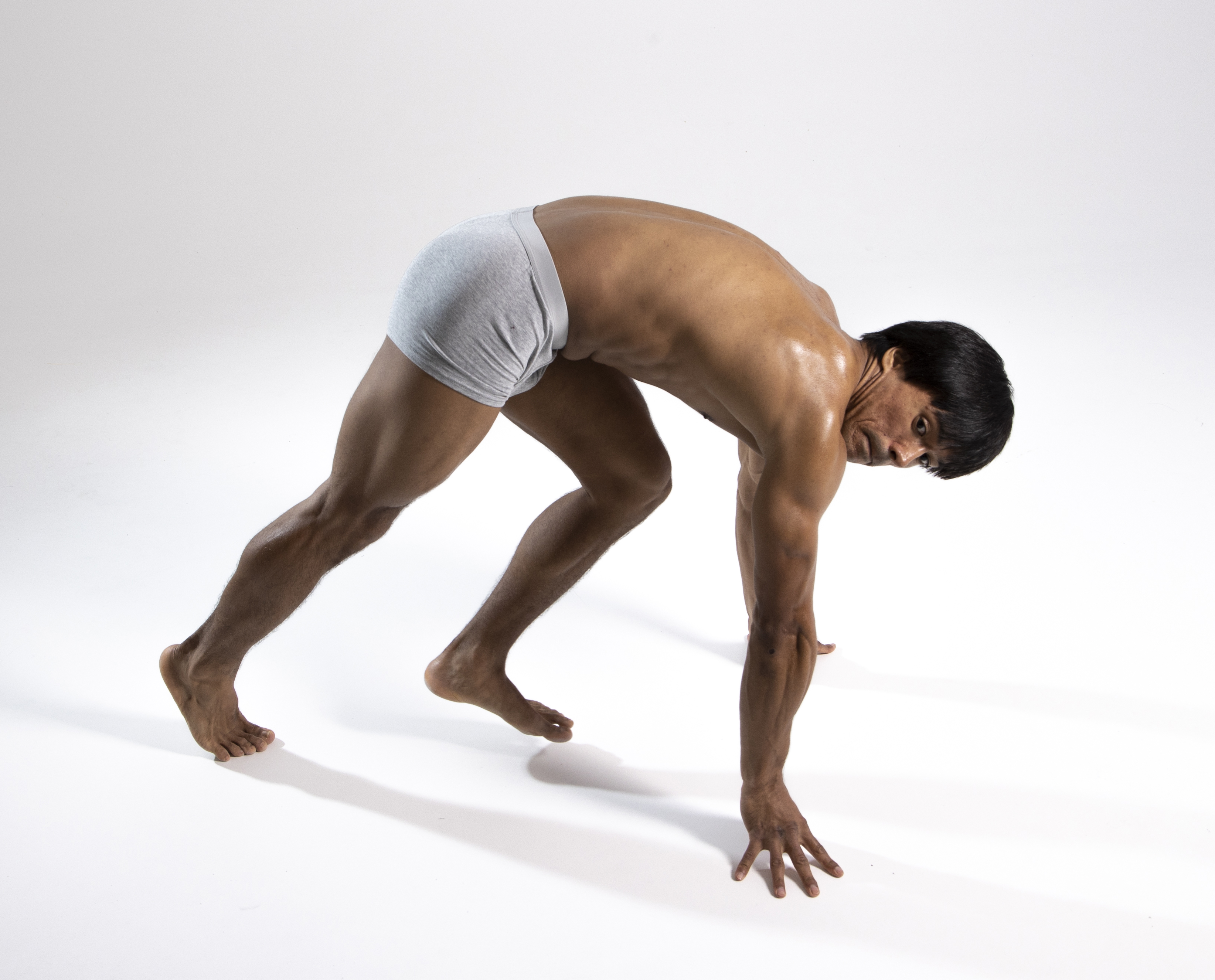 a muscular man wearing underwear is in a crouching position on a white surface, with his hands and feet touching the ground, as if getting ready to start a race.