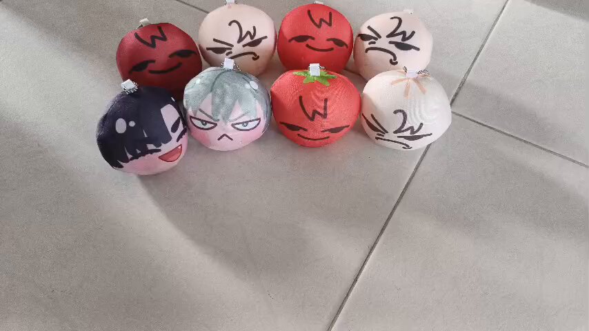 a collection of plush toys in the shape of round mochi with different character faces. they are red, white, pink, and have cute anime/mangastyle facial expressions on them.  these toys are soft, squishy, and very appealing.