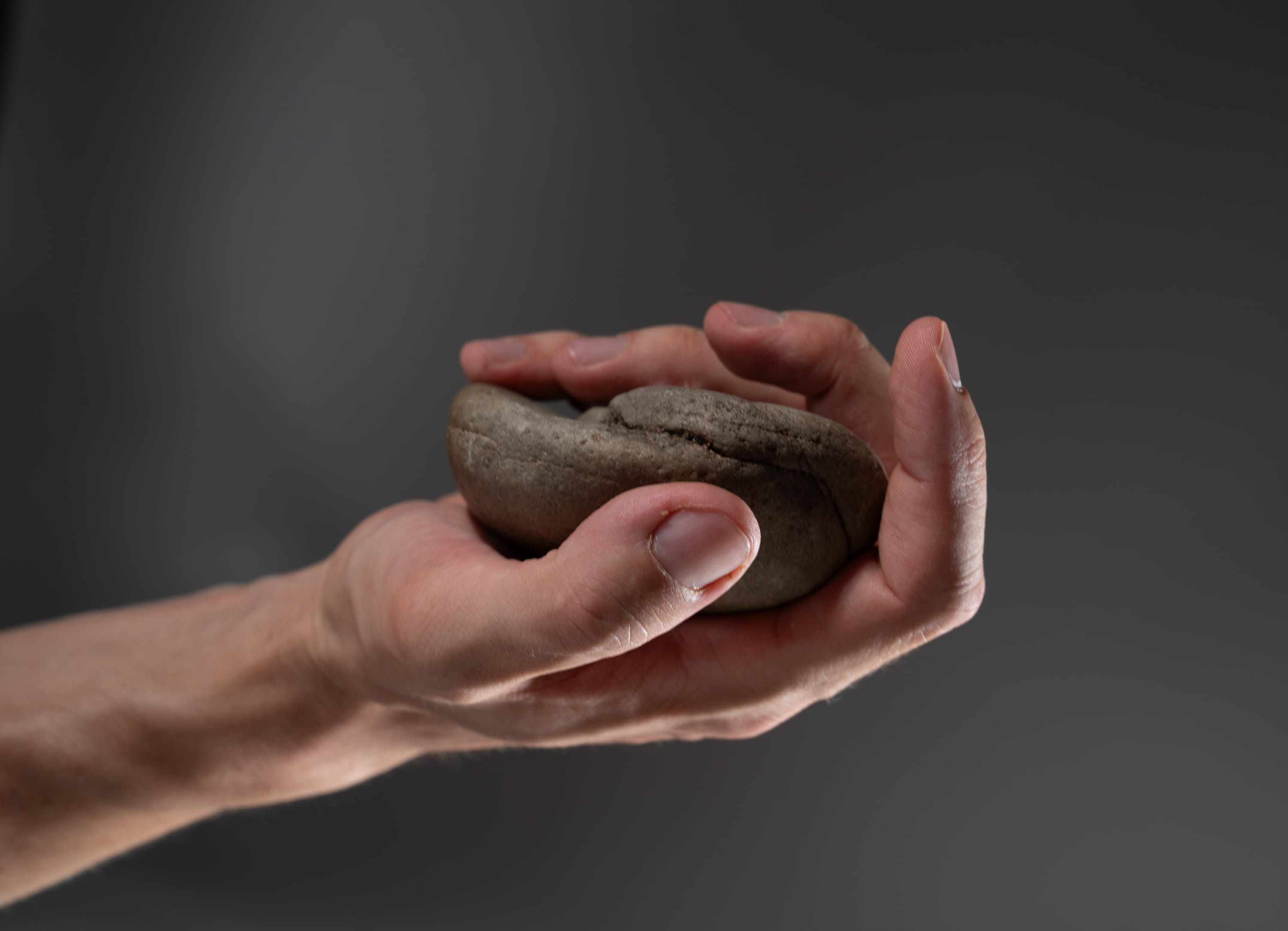 a photo of a man's hand holding a gray rock with a dark gray background.