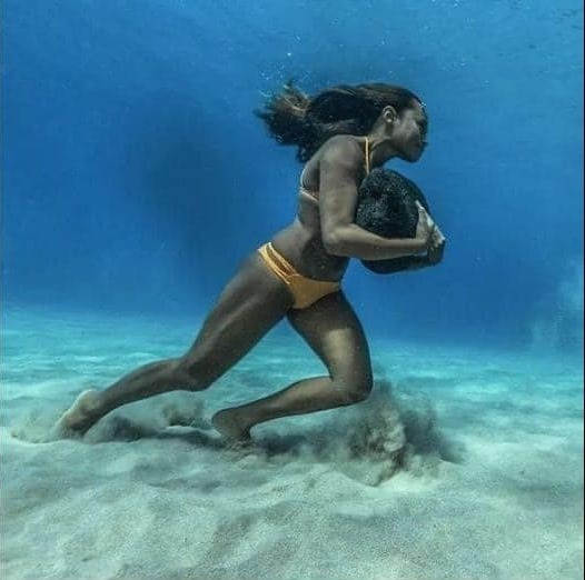 a woman in a yellow bikini swims underwater, holding a large rock in her arms. she is strong and powerful, with a determined expression on her face. the water is clear and blue, and the sand is white and powdery.  the image is a beautiful and powerful depiction of human strength and the beauty of the natural world.