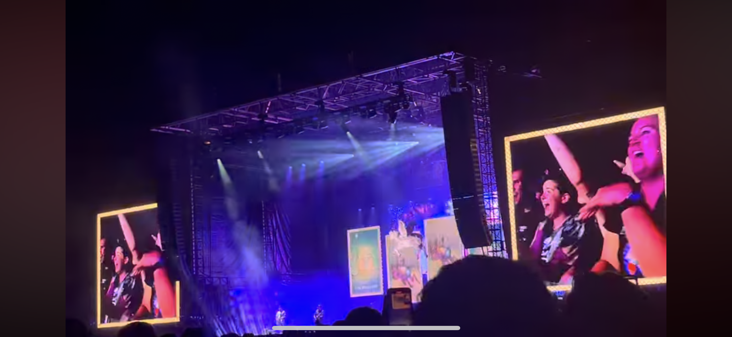 a live concert performance is captured during the night. the stage is brightly lit with spotlights and surrounded by excited fans. the crowd is cheering and dancing to the music, enjoying the energy and excitement of the event. two large screens display images of the performers, capturing the essence of the live show.
