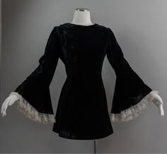 a black velvet dress with bell sleeves and lace trim. the dress is a vintage style, likely from the 1960s or 1970s. it is a short dress, with a fitted bodice and a flared skirt. the sleeves are long and bellshaped, with a lace trim at the bottom. the dress is a classic style that is perfect for a party or a special occasion. the dress is modeled on a mannequin and is shown from the front. the background is a plain white wall.