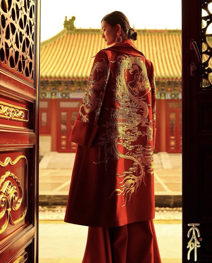 a woman wearing a red robe with dragon embroidery stands in front of an oriental building. the building has a traditional chinese architectural style, with a goldcolored roof. the woman is wearing a red robe with intricate golden dragon embroidery. she is standing near a door, which is partially open.