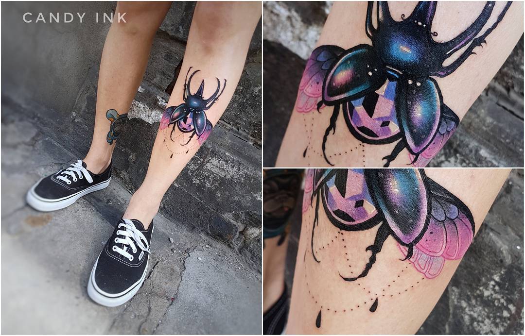 the image is a collage of three photos showcasing a neotraditional tattoo of a beetle on the back of a person's calf. the beetle is depicted with its wings spread, showcasing a mesmerizing, colorful geometric pattern within its body. the wings are rendered with delicate pink hues and intricate details. the overall tattoo is vibrant and eyecatching, reflecting a modern take on traditional tattoo styles.  the person is wearing black canvas shoes.