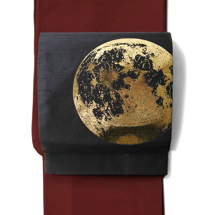 an image of a folded kimono. the kimono is red with a black obi with a large gold moon design.