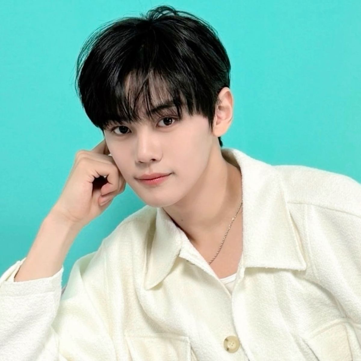 a head and shoulders shot of a young asian man with dark hair and brown eyes. he is wearing a white collared shirt and posing against a turquoise background. the image appears to be a professional headshot, possibly for a singer or entertainer.