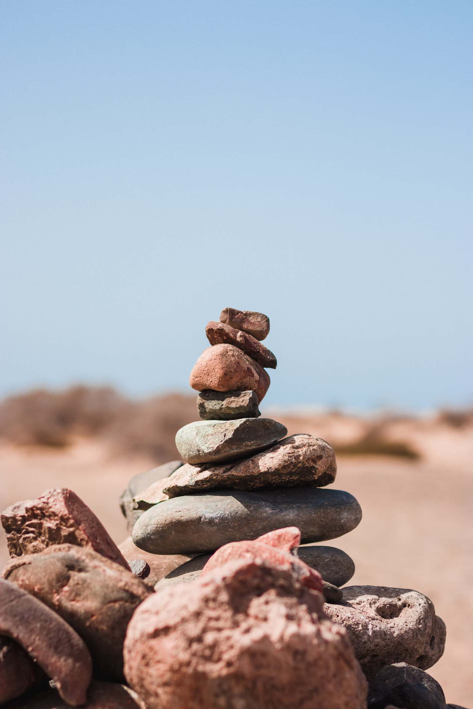 a stack of carefully balanced rocks in the middle of a desert landscape sits under a bright blue sky.