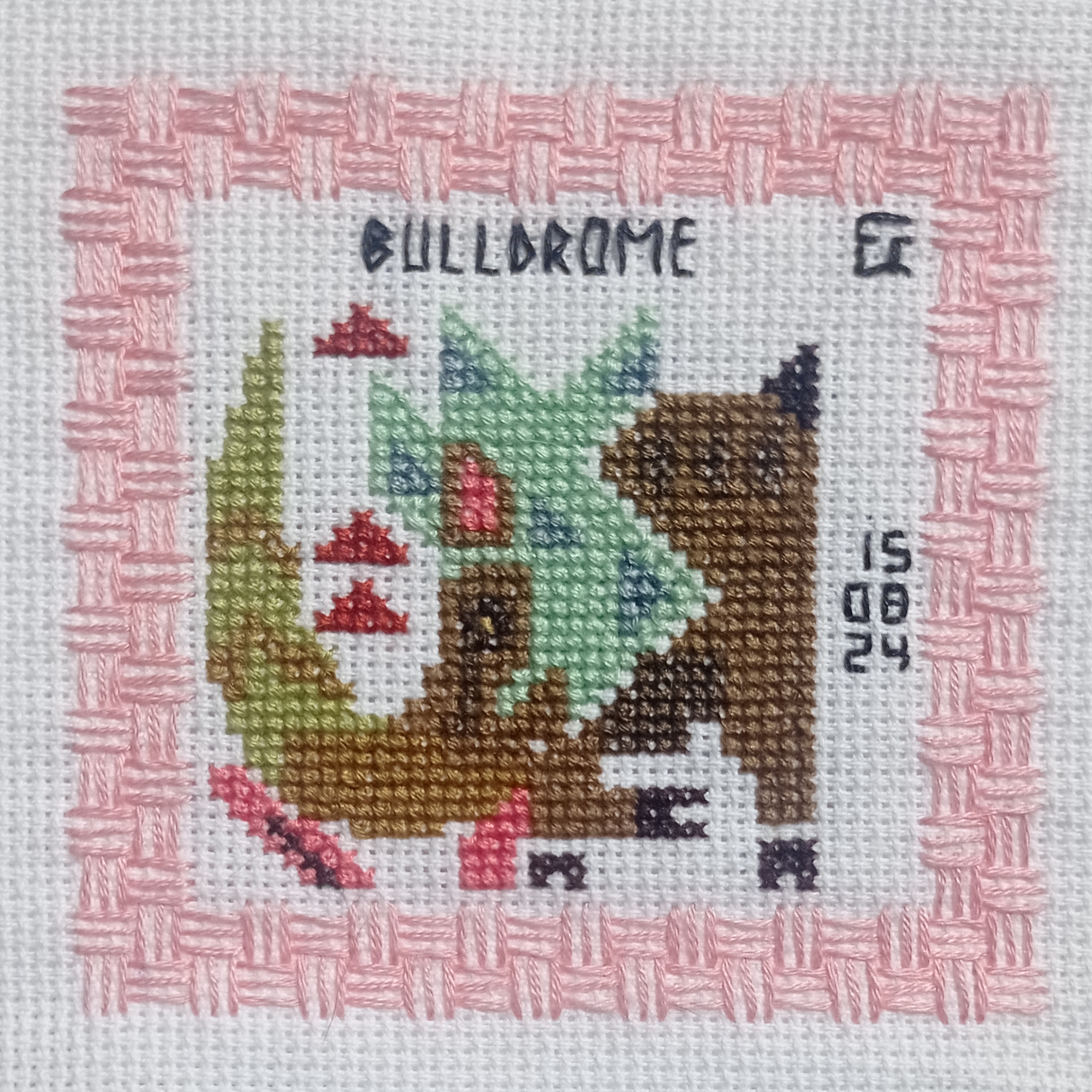 a crossstitch artwork of a stylized rhino in profile (facing right) with a green horn, brown body, and colorful accents.  it's framed with a pink border and includes the words "bullorome" and "08 24" stitched above and below the rhino.