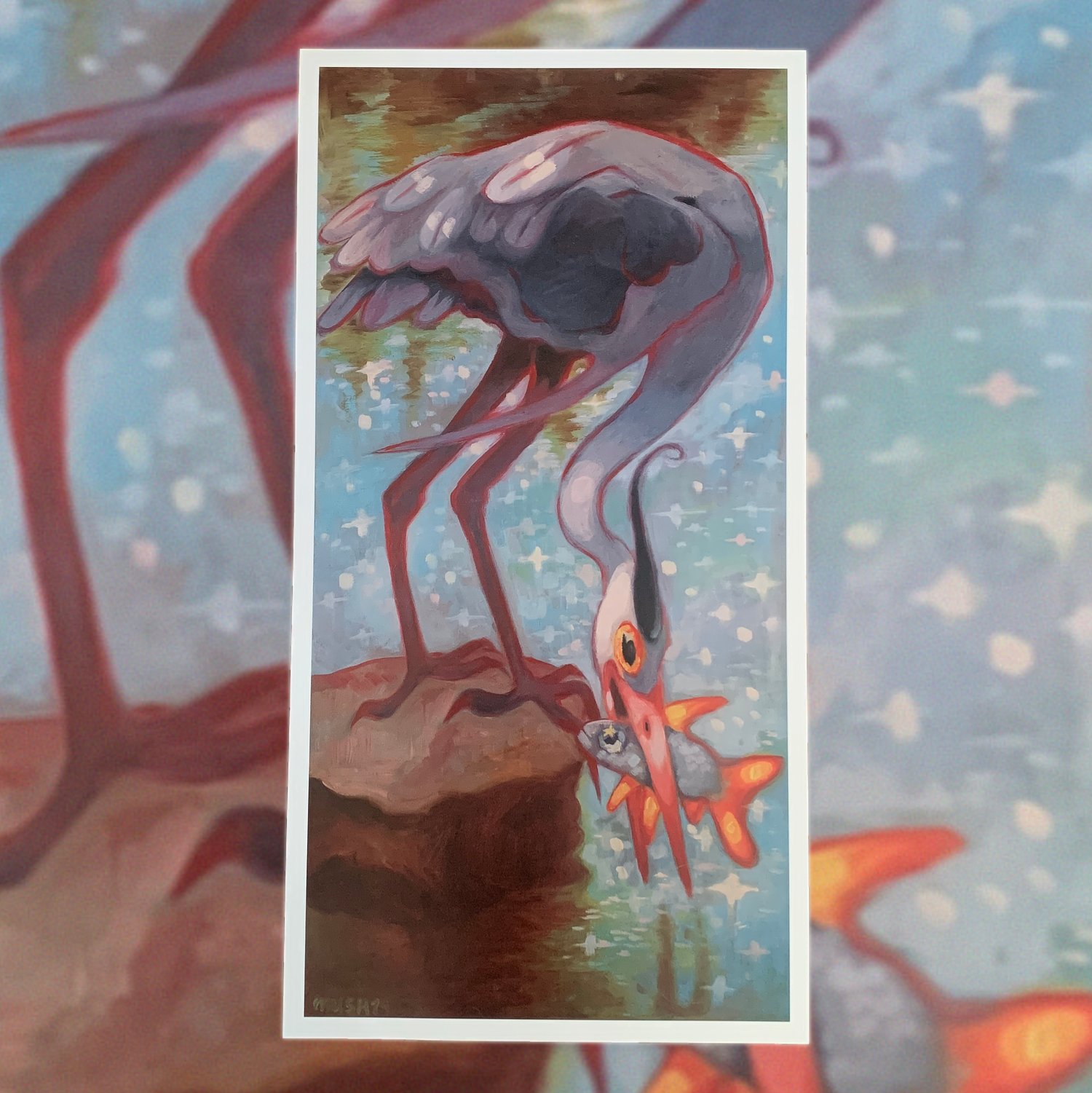 the image shows a closeup view of an art print featuring a stylized painting of a great blue heron. the heron is depicted in a slightly whimsical style, with rich, saturated colors. it's positioned bending down, its beak piercing into the water, catching an orange and red fish. the heron's plumage is detailed, showing shades of gray, blue, and purple. the background suggests a tranquil watery setting with shimmering reflections, and a rock provides a focal point near the heron's feet. the overall style is a blend of realism and fantasy, giving the painting a magical or dreamlike quality. the print is displayed against a blurred background that appears to be more of the same artistic style.