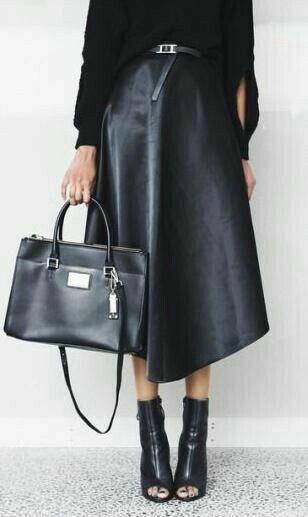 the image showcases a woman elegantly dressed in a monochrome outfit. she's wearing a black, longsleeved sweater, paired with a black leather midi skirt that falls to midcalf. the skirt is aline in shape with a slight asymmetry. she's also wearing black ankle boots with a peep toe.  completing the look is a black structured tote bag, carried by the woman. the overall style is minimalist and chic, reflecting a fall or autumn fashion aesthetic. the setting appears to be a simple, lightcolored interior.