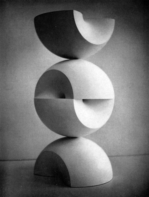 a black and white photograph shows a sculpture made of stacked geometric shapes. the sculpture consists of three main components: a halfsphere at the bottom, a sphere in the middle that has a horizontal cutout section, and another halfsphere on top. the shapes are stacked on top of each other, creating a balanced and abstract composition. the image is minimalist in style, focusing on the interplay of light and shadow on the smooth surfaces of the geometric forms.