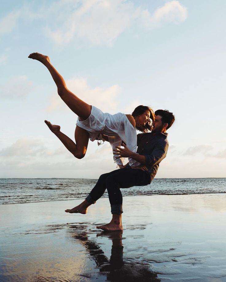 a couple is playfully dancing on the beach at sunset. the woman is