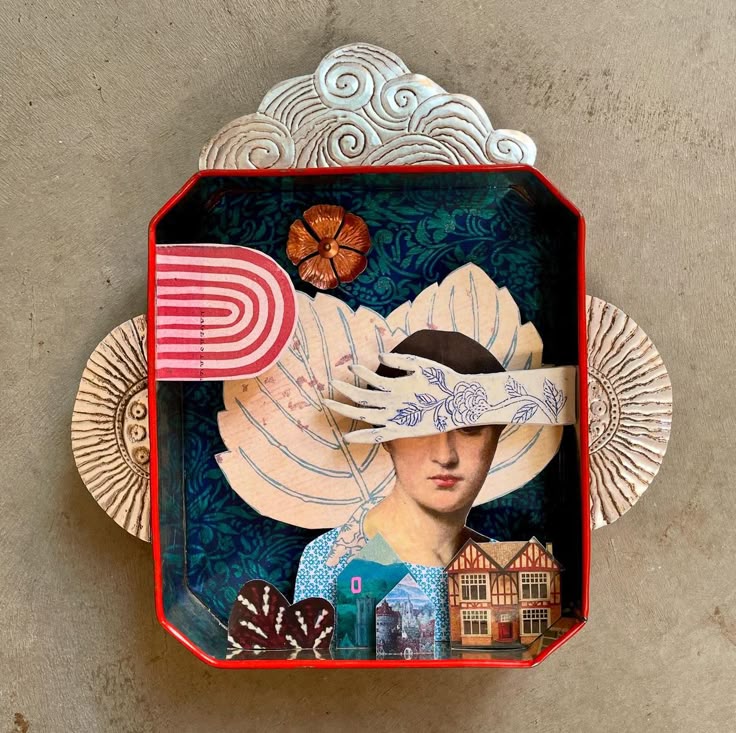 a mixed media assemblage features a portrait of a woman with a hand acting as a blindfold. the collage includes elements like a flower, a rainbow, miniature houses, and a cloud motif at the top. the background features a floral pattern. the artwork is framed in a rededged box with decorative elements on the sides.